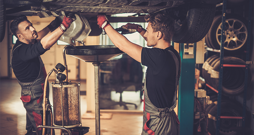 Mechanics draining oil from under a car during a service